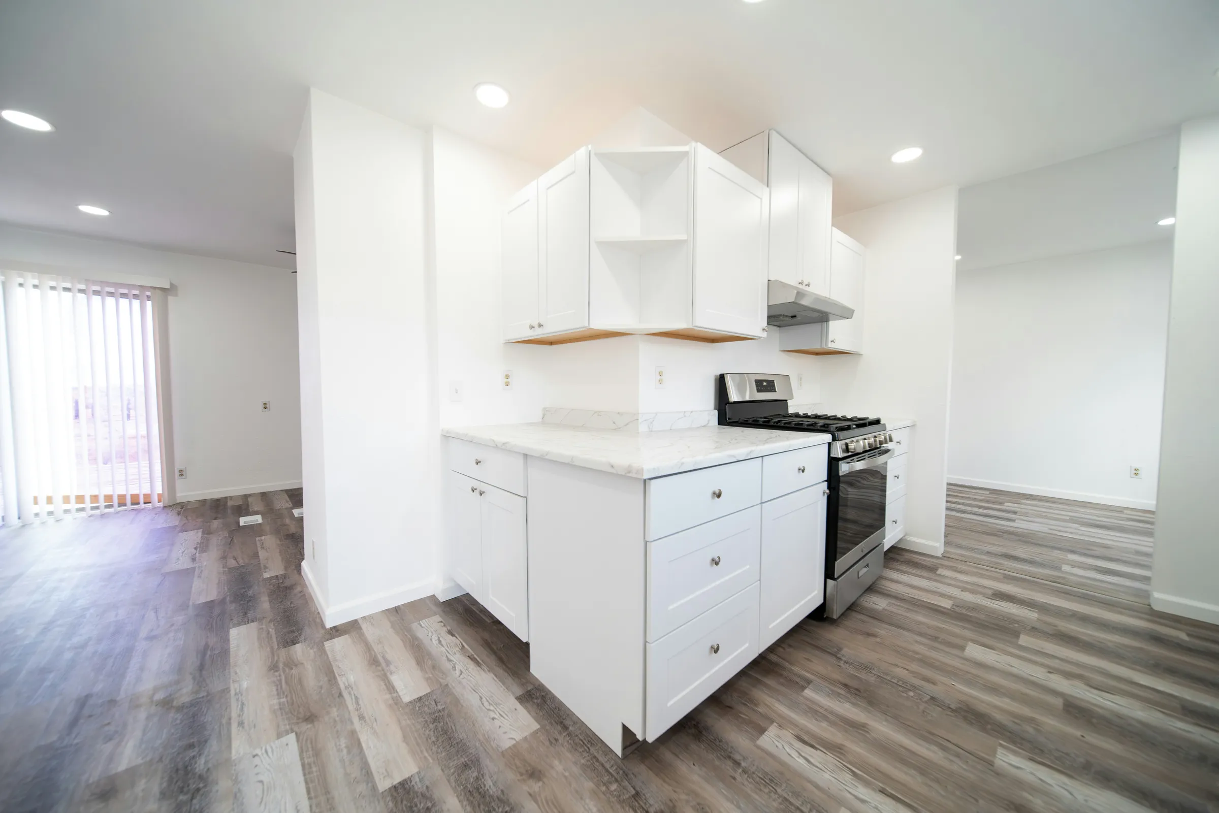 Stock photo: a run of white shaker-style cabinets with a marble-look countertop and a stainless gas range in an empty room with grey plank flooring